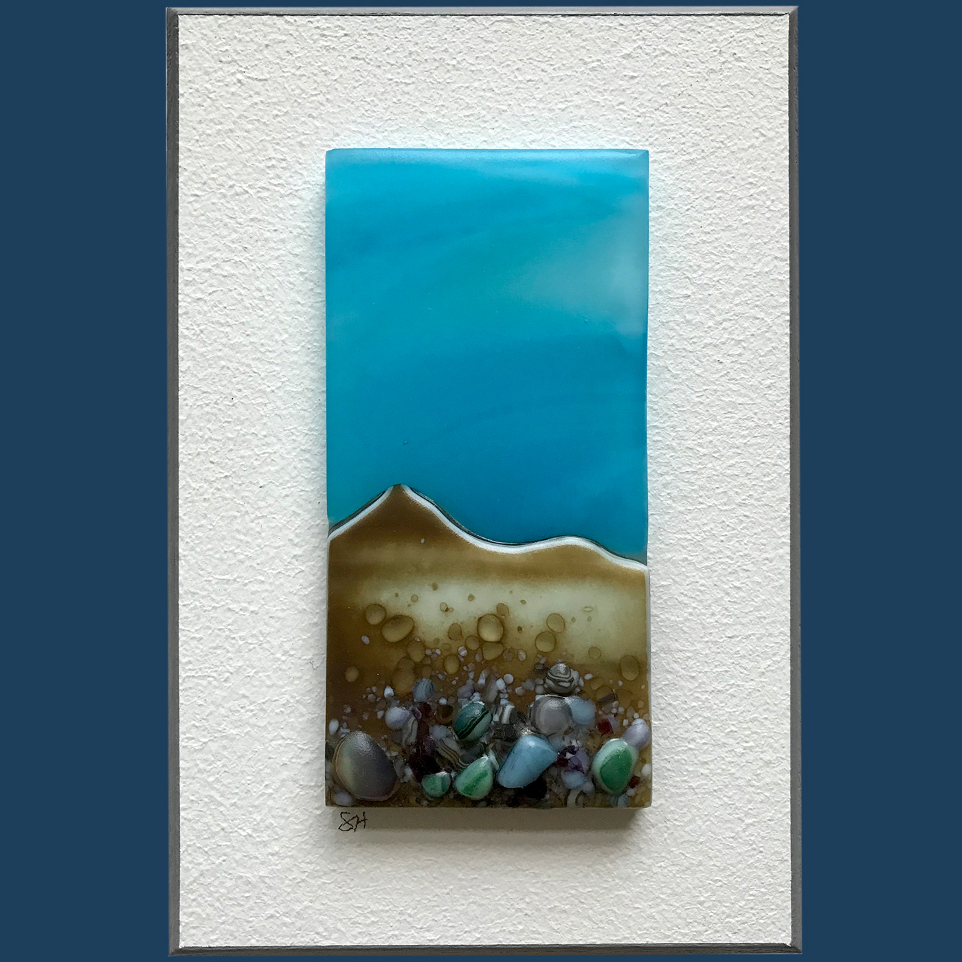 Seascapes fused glass wall art, welsh coastal landscapes, blue sky, vanilla/grey/green/brown/lilac glass frits in foreground.